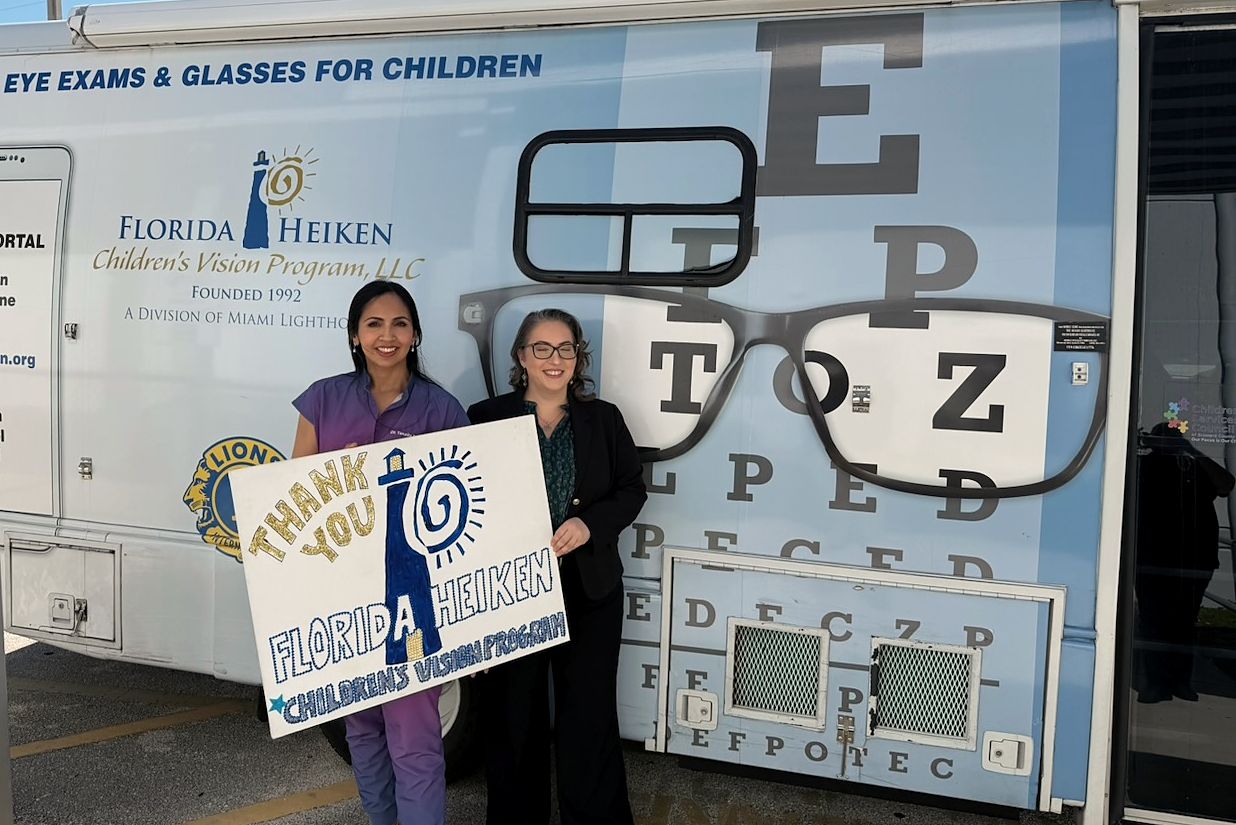 Dr. Rahman beside the Florida Heiken Children's Vision Program van, painted with an eye chart, holding a thank-you sign.